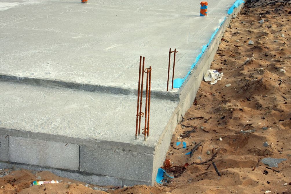 Dalle de béton partiellement construite avec armatures apparentes à côté d'une tranchée de terre.