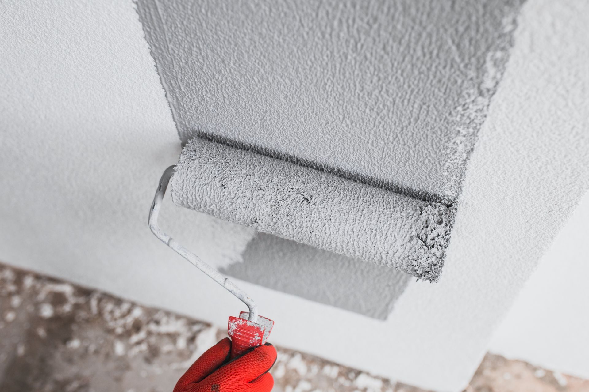 Une main peint un mur blanc au rouleau.