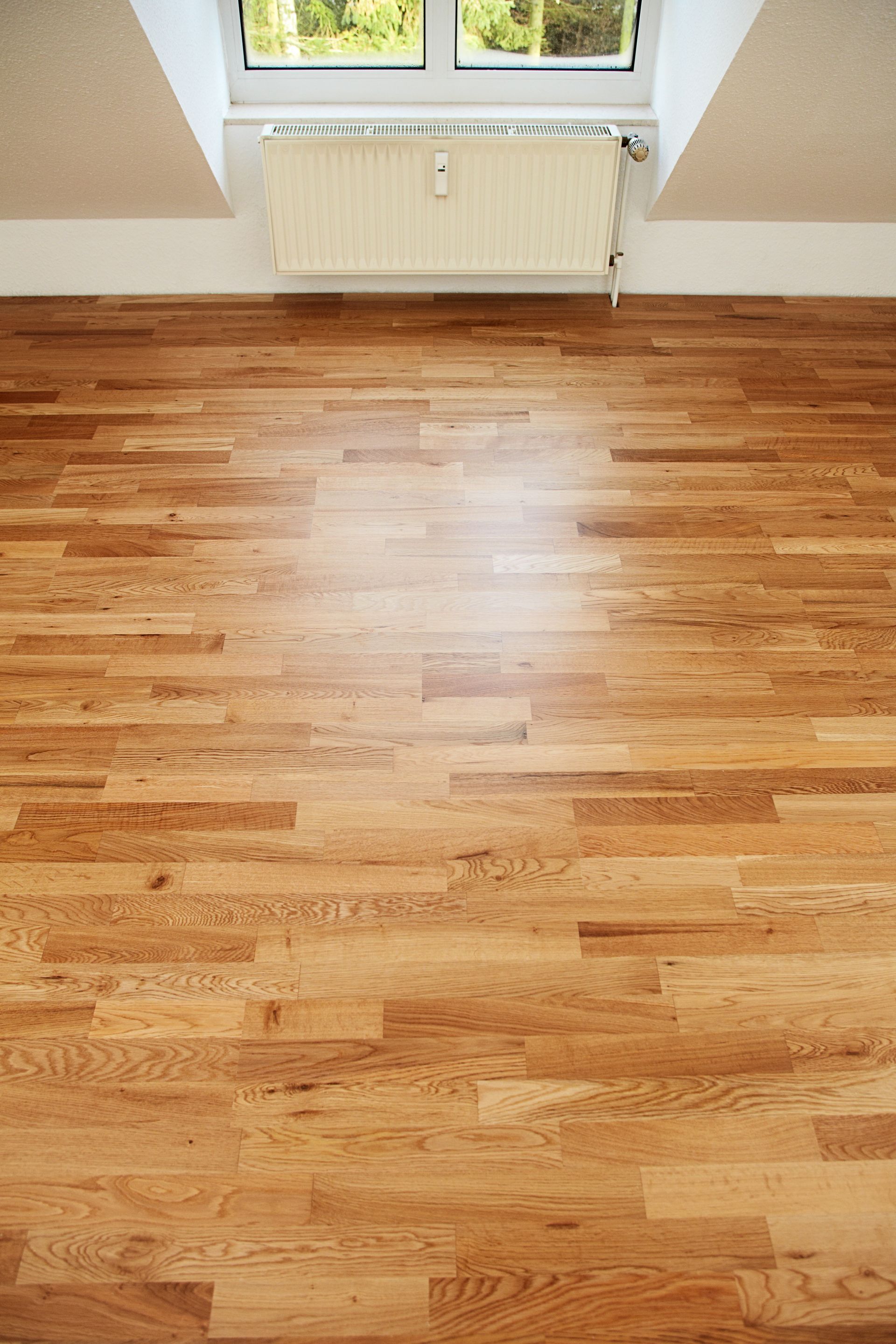 Pièce vide avec parquet ciré, murs blancs, fenêtre et radiateur sous la fenêtre.