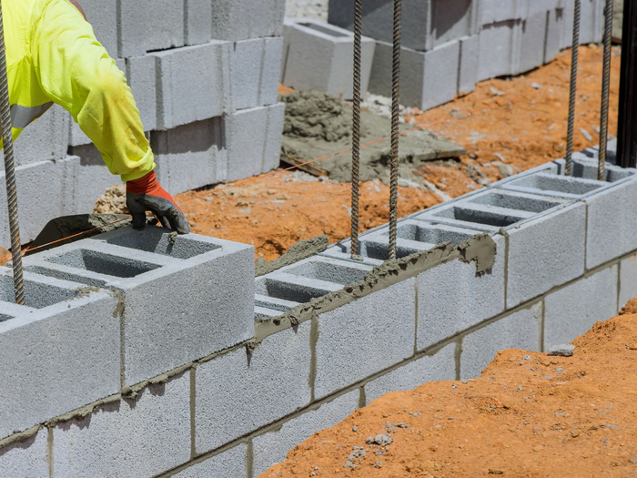 Un ouvrier pose des parpaings pour un mur de fondation sur un chantier de construction.