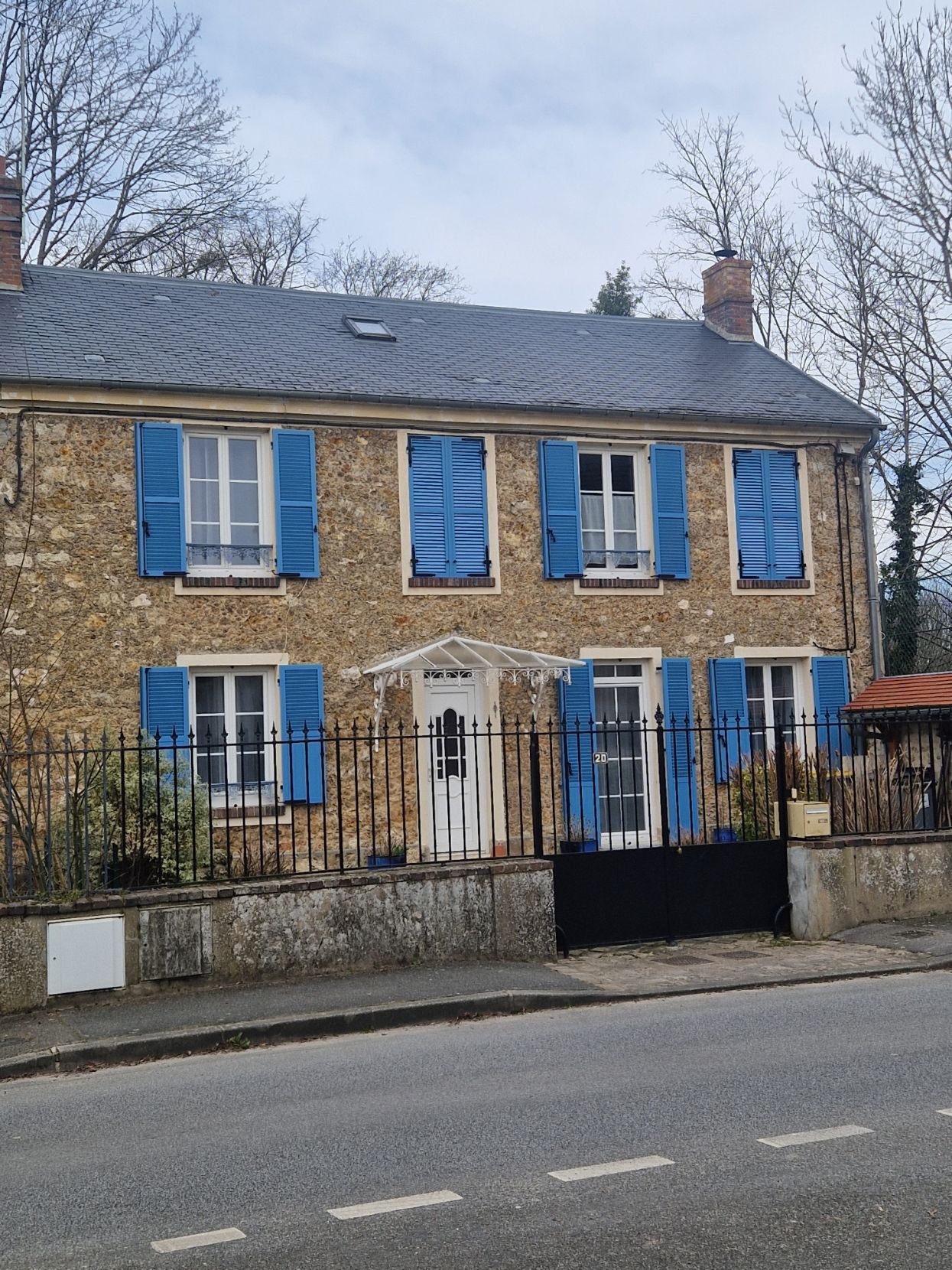 Maison avec de nombreuses fenêtres avec des volets bleus et une porte d'entrée blanche