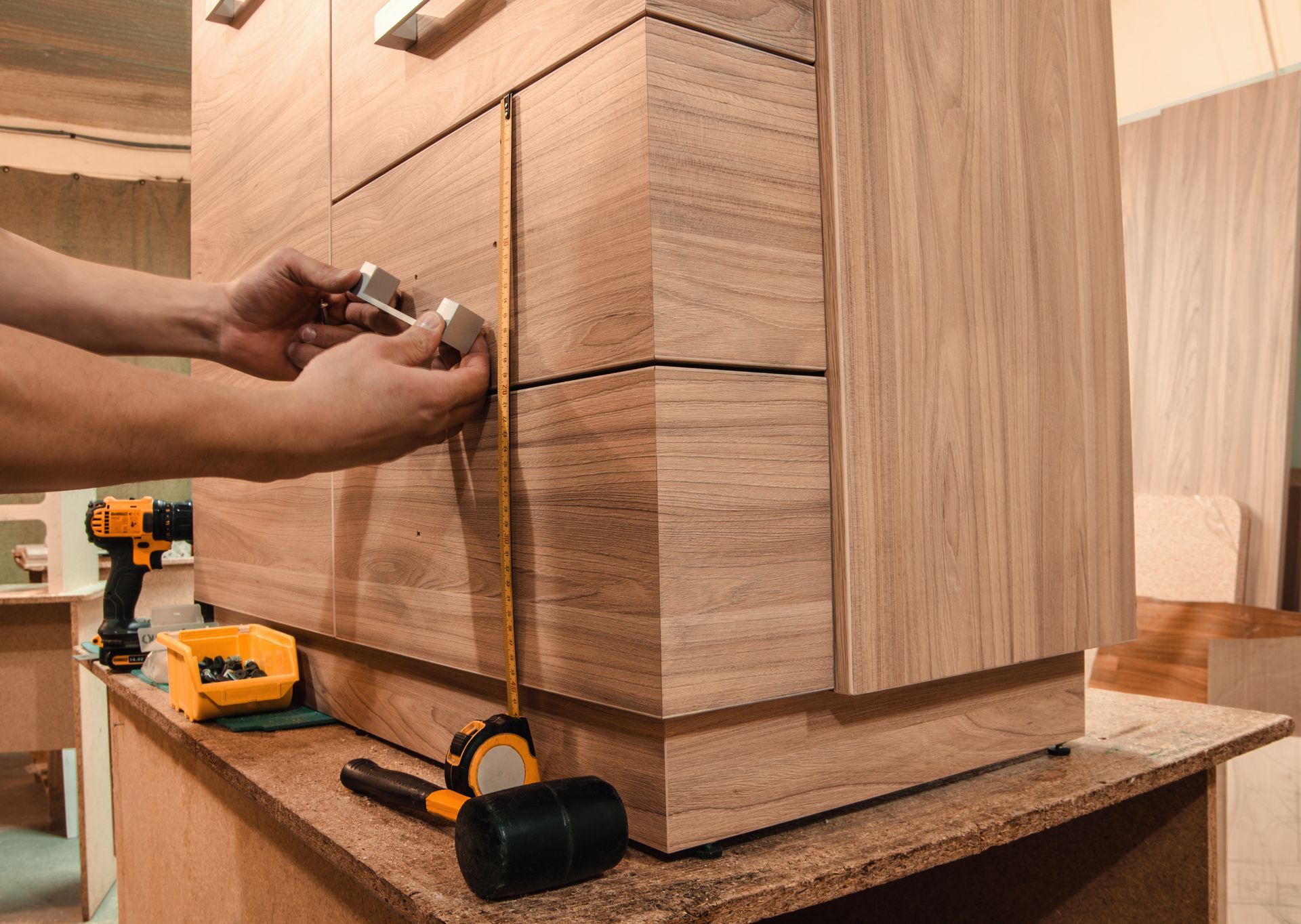 Professionnel prenant des mesures sur un meuble en bois sur lequel il fixe des poignées