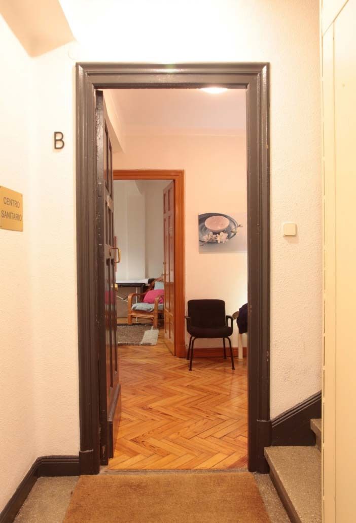 Puerta de entrada al interior de un edificio con pasillo y habitaciones; piso de madera, paredes y obras de arte.