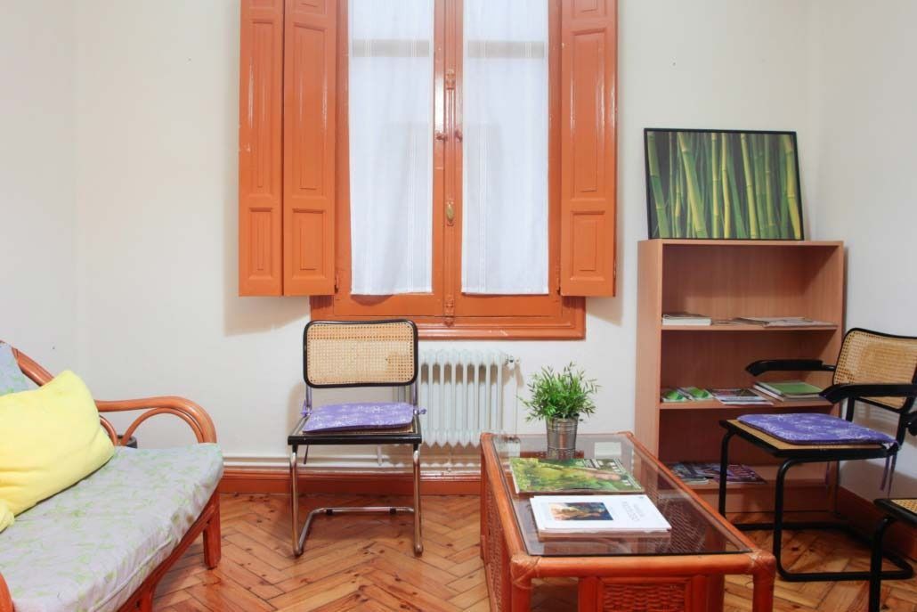 Sala de estar con persianas naranjas, un pequeño sofá, sillas y una estantería.