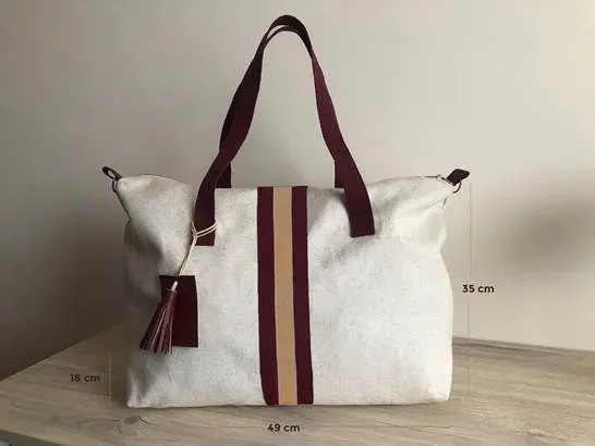 Un bolso de mano blanco con una correa de rayas burdeos y tostado está sobre una mesa de madera.