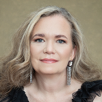 Mujer con cabello rubio ondulado, con top negro y pendientes, sonriendo.