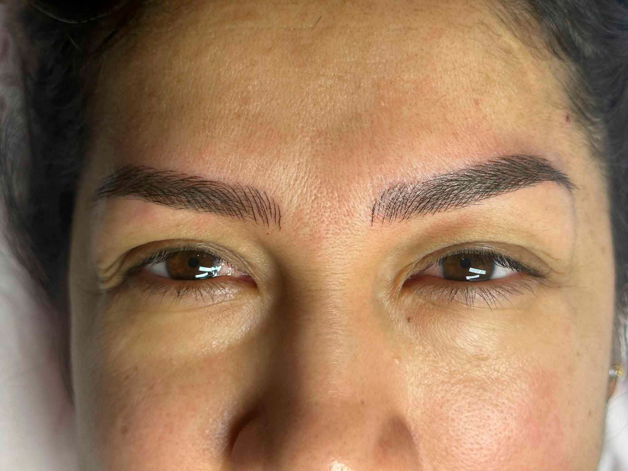 Un primer plano del rostro de una mujer con un tatuaje en las cejas.