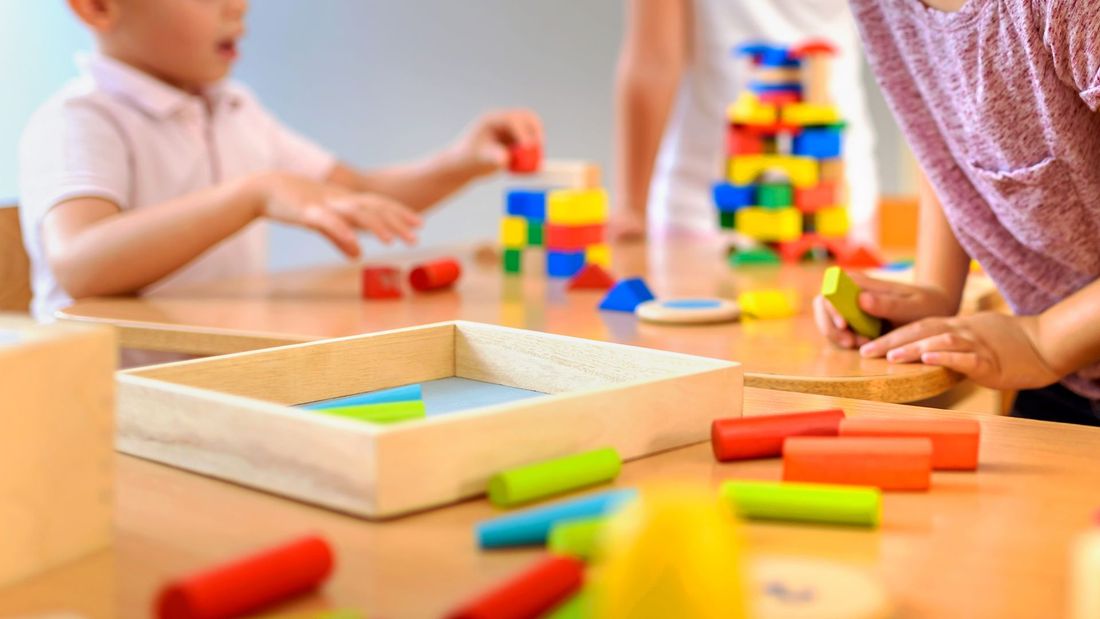 Kinder spielen in einem hellen Spielzimmer an einem Tisch mit bunten Bauklötzen.