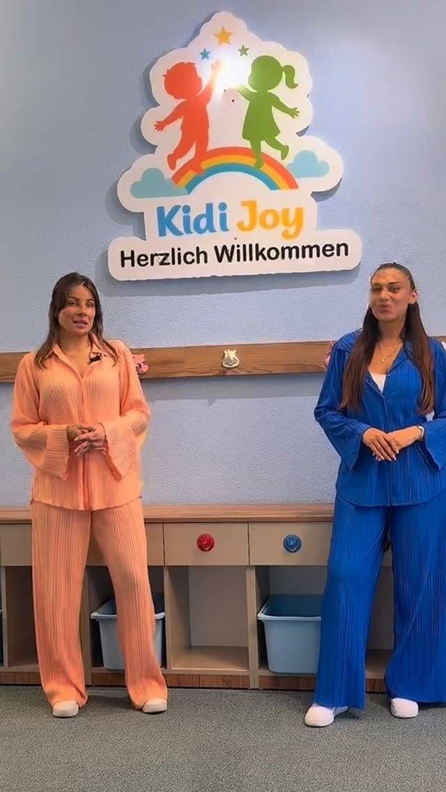 Zwei Personen stehen neben einem Willkommensschild von KidzJoy in einem hellen Innenraum.