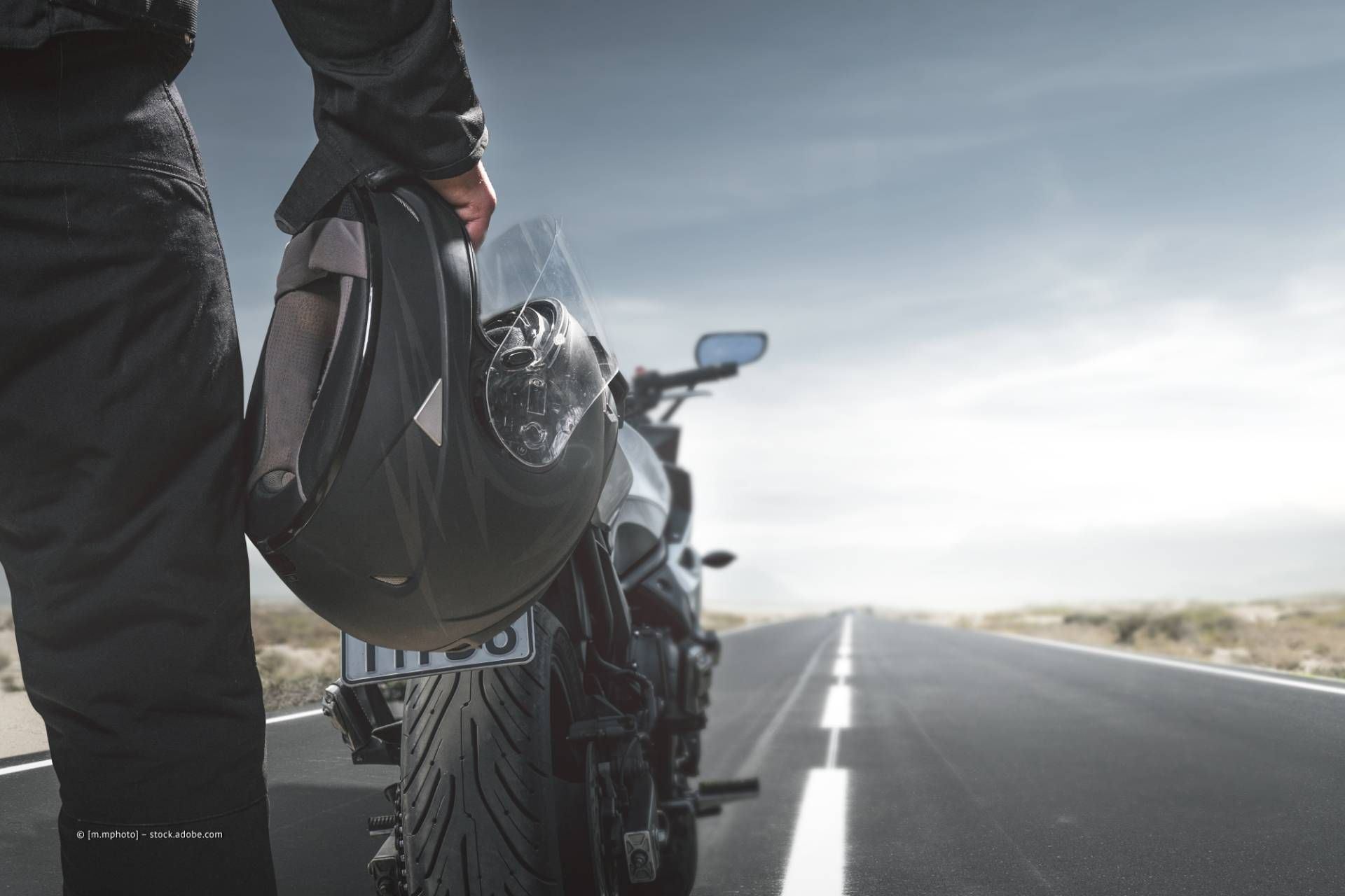 Motorradfahrer mit Helm in der Hand auf einer Straße