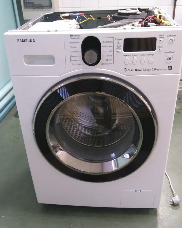 Machine à laver Samsung blanche à chargement frontal, panneau supérieur ouvert, laissant apparaître des fils électriques.