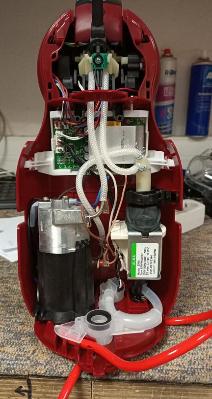machine à café rouge ouvert avec câblage, moteurs et tubes apparents sur un établi