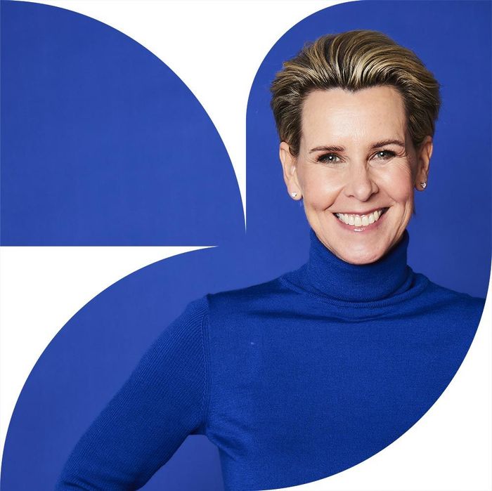 Eine Frau in einem blauen Rollkragenpullover lächelt vor einem blauen Hintergrund