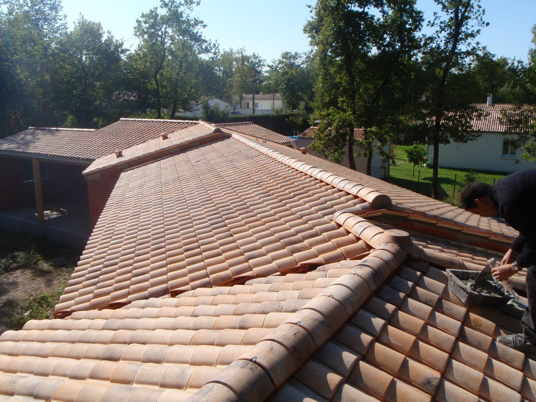Un couvreur travaille sur un toit de tuiles en terre cuite.