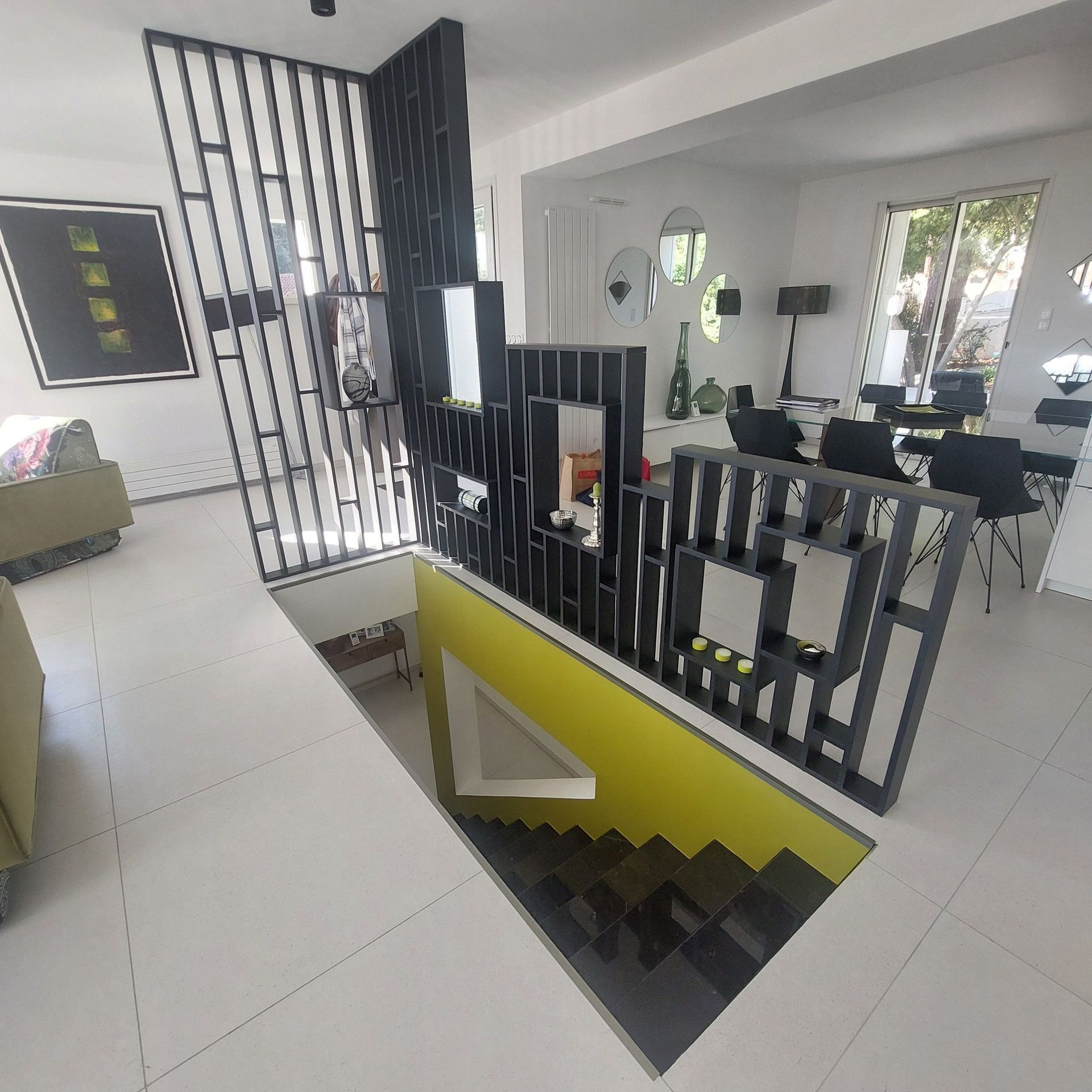 Intérieur moderne avec escalier ouvert, paravent noir géométrique.