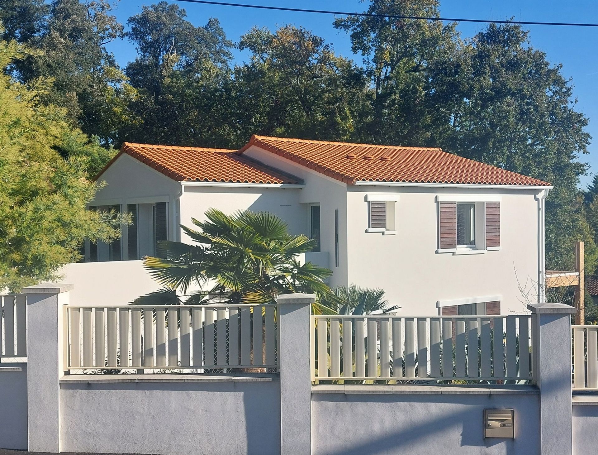 Maison à étage aux murs blancs, toit de tuiles et clôture blanche.