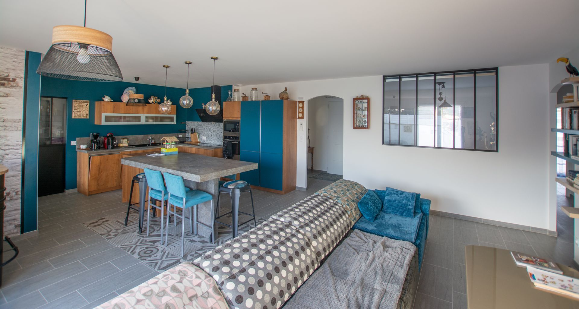Cuisine en bois aux murs bleus ouverte sur un salon, verrière au mur
