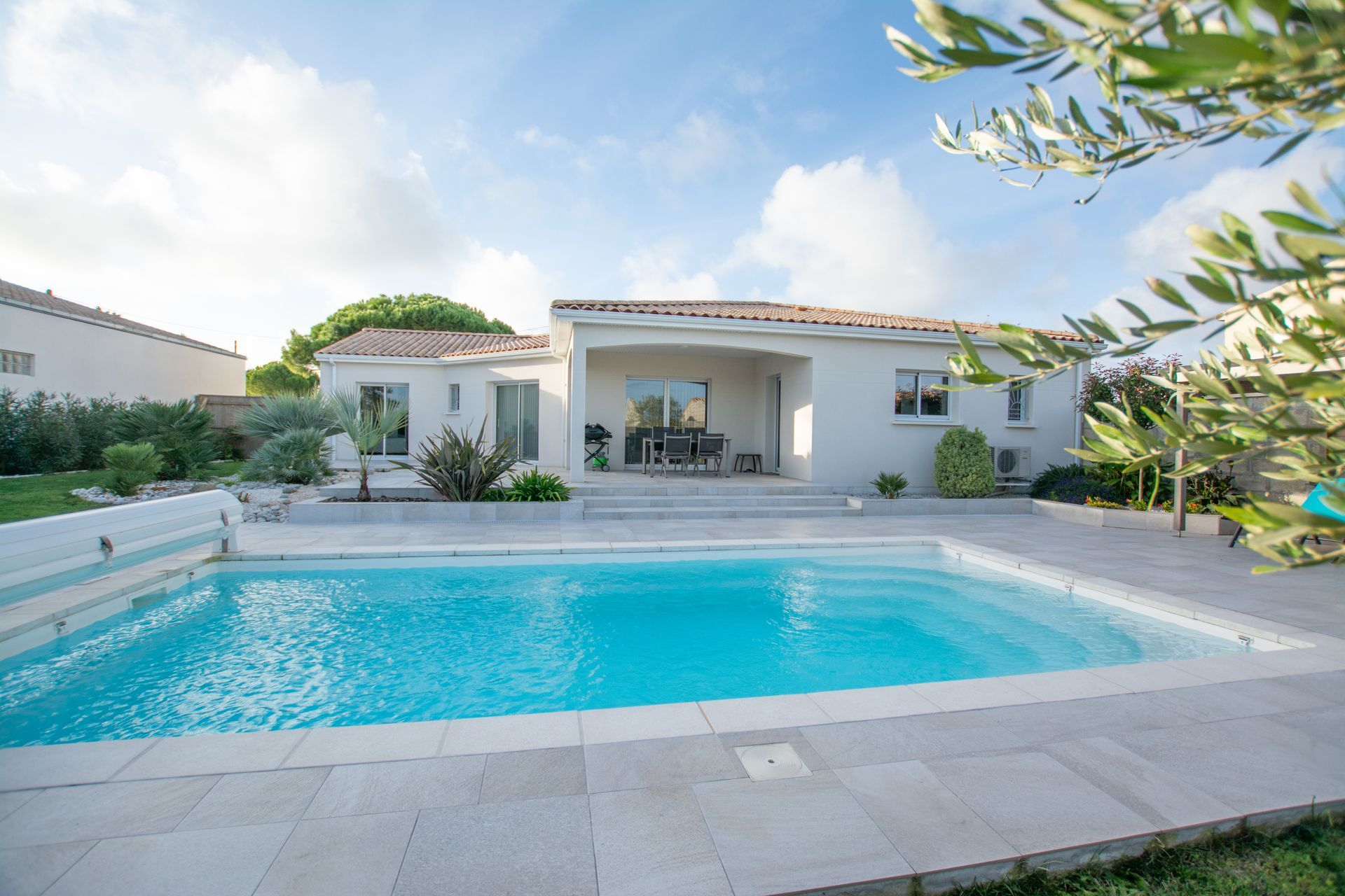 Piscine devant une maison claire avec terrasse.