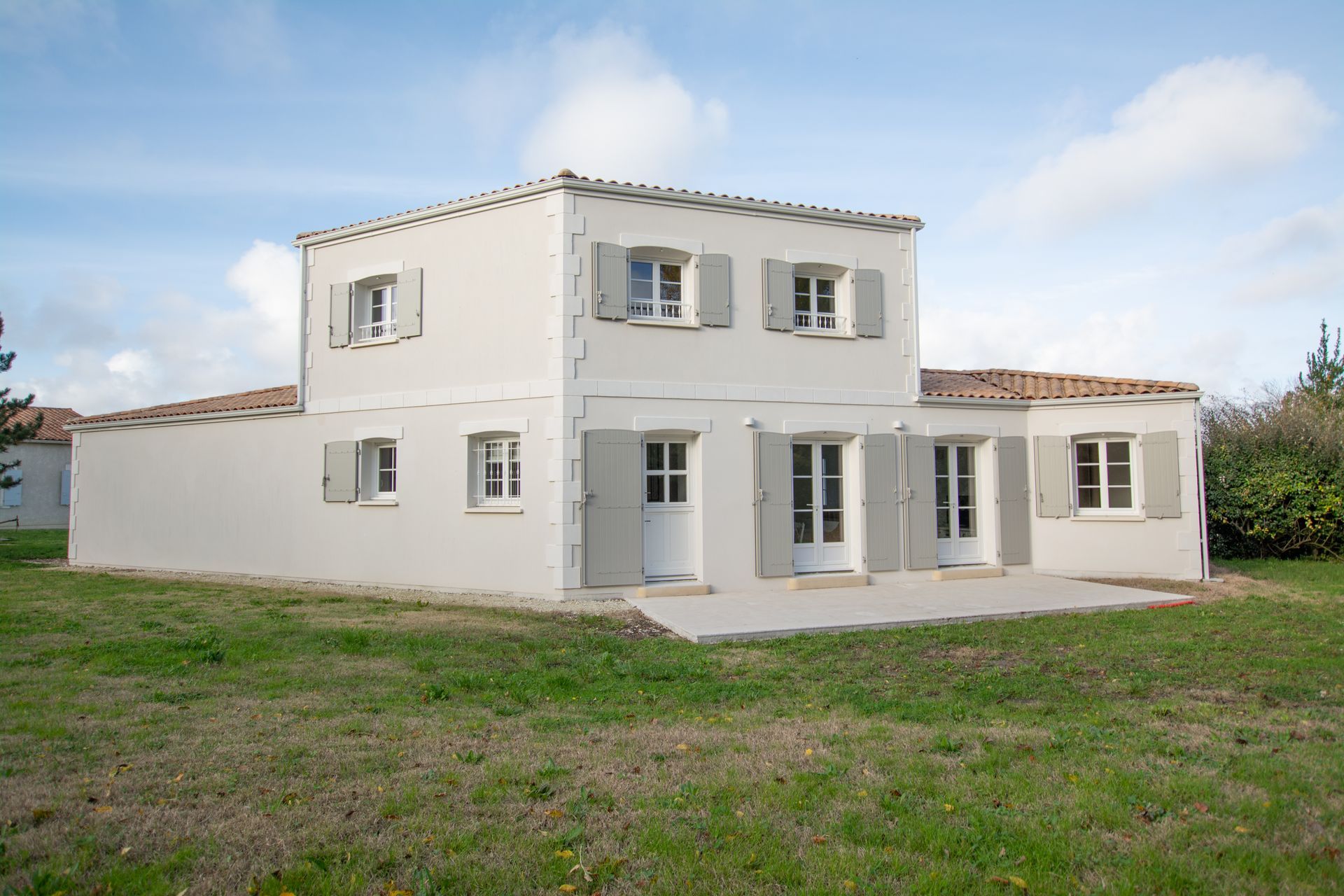 Maison blanche à deux étages avec des volets gris et un toit plat.