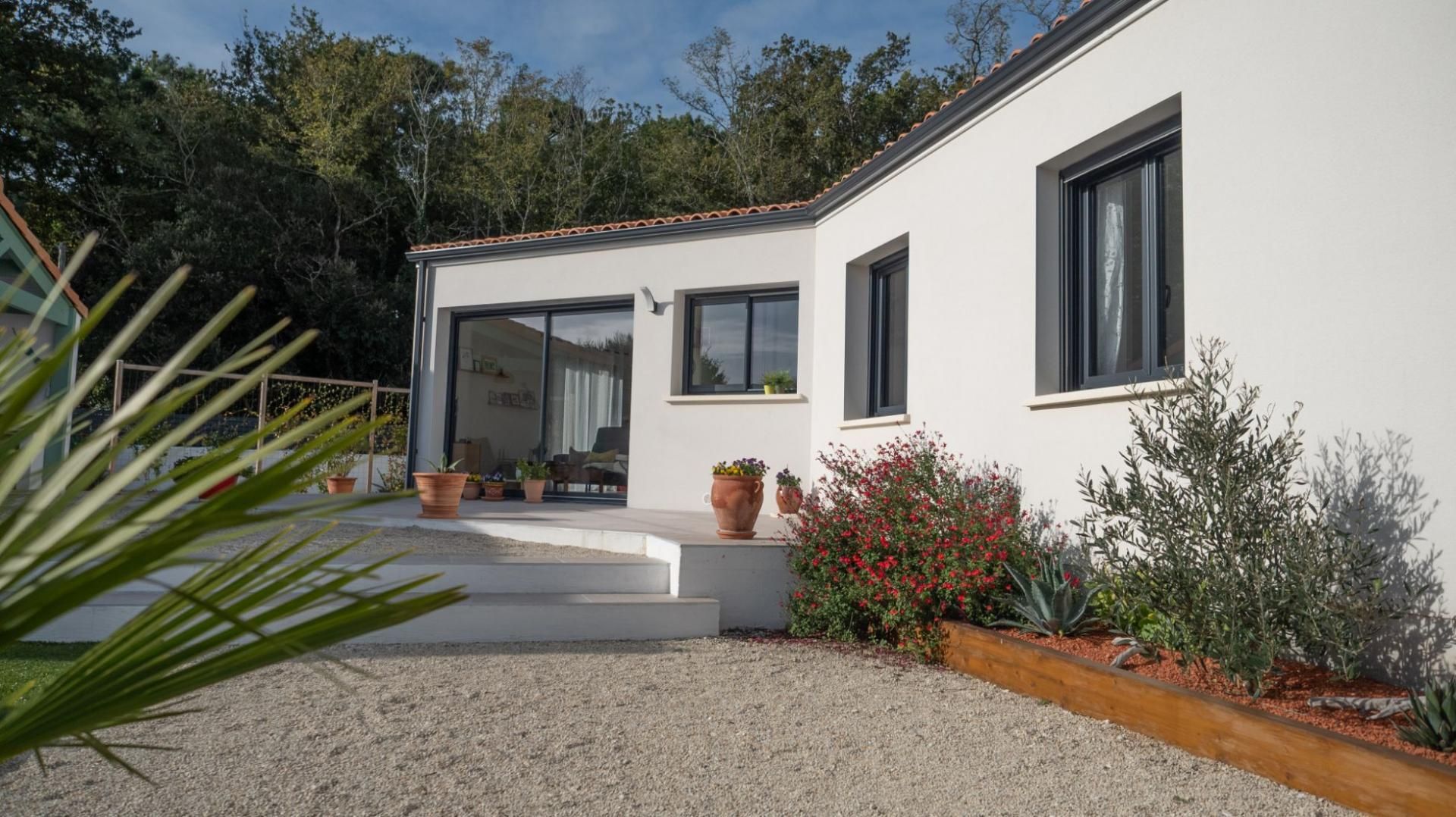 Maison blanche et cour en gravier, marches et verdure.