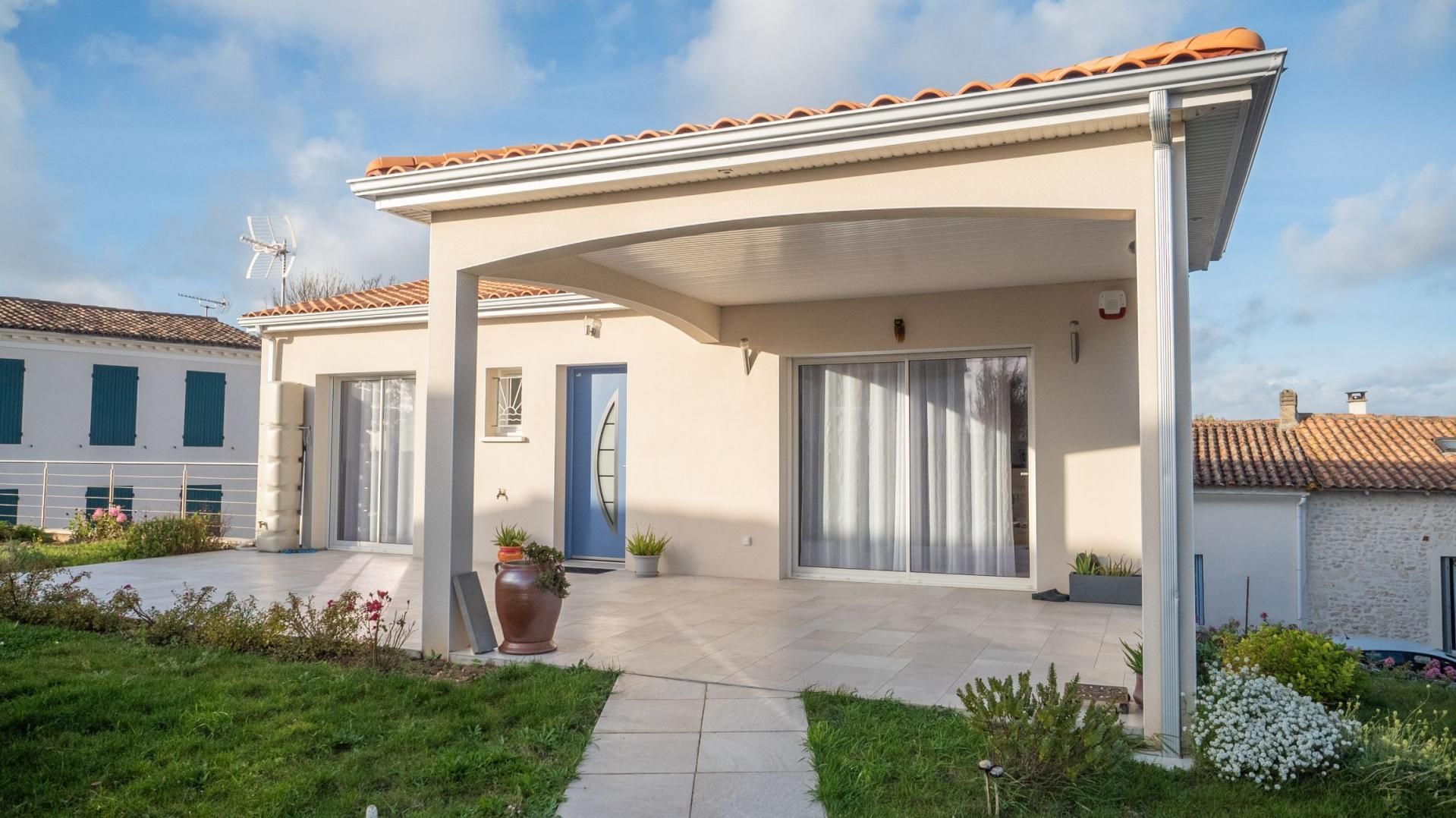Maison beige avec patio couvert, porte bleue et toit en tuiles.