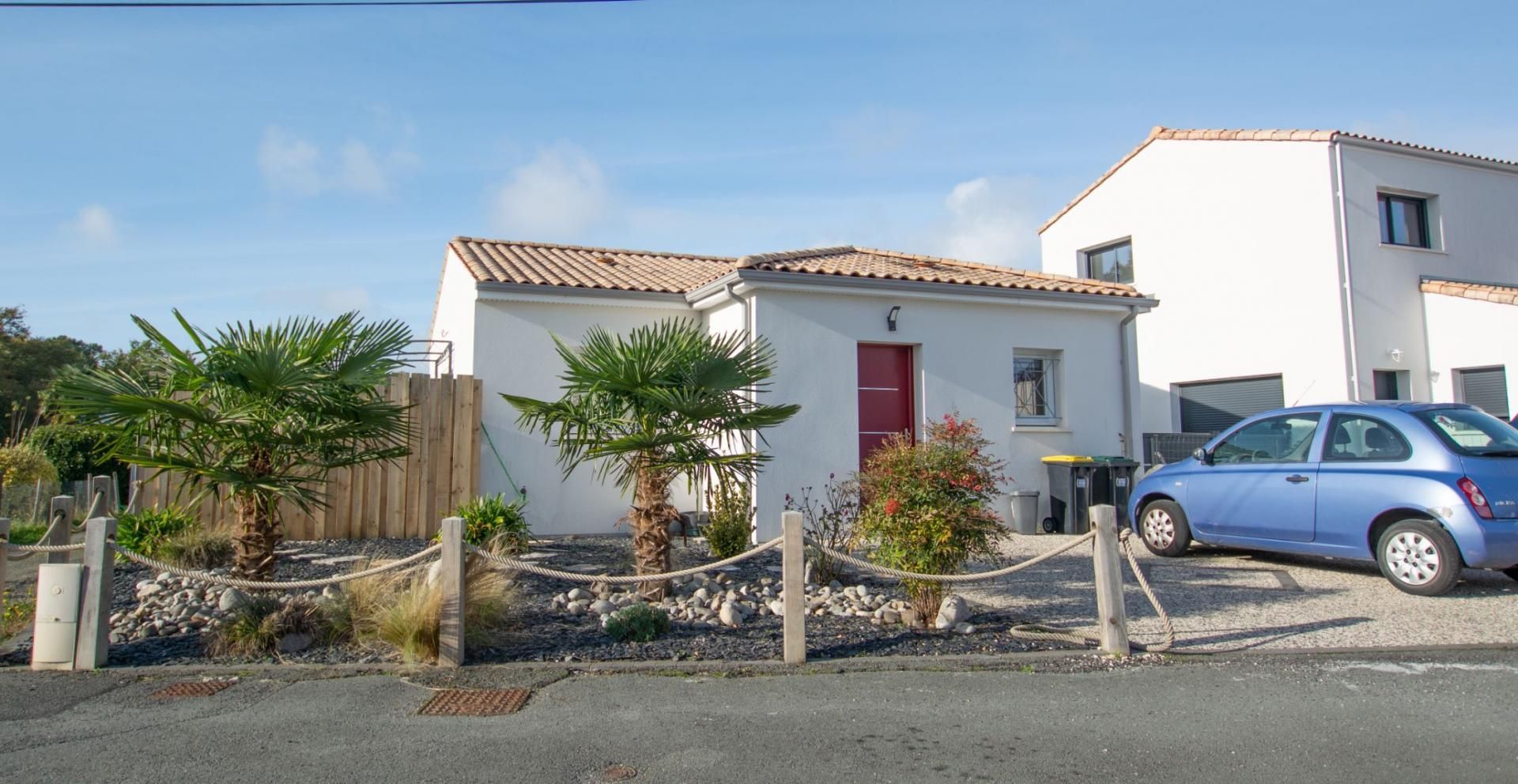Maison blanche à porte rouge. Palmiers et clôture devant.
