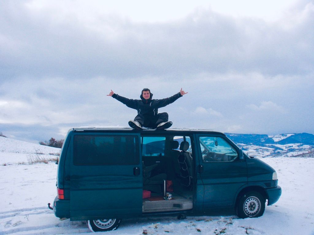 Un homme assis sur son van fait le symbole des surfeurs avec ses mains