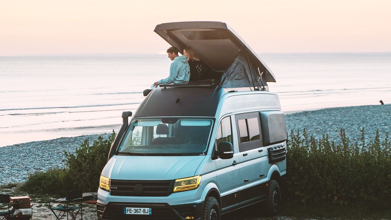 Un couple assis sous le toit relevable de son van regarde la mer