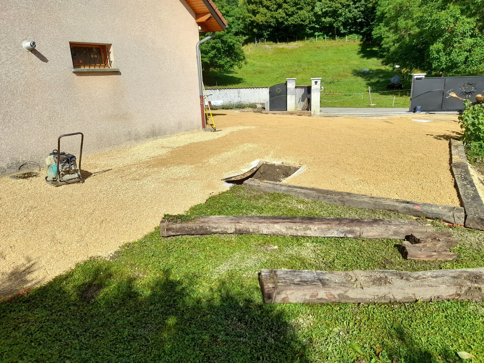 Préparation d'une allée de gravier à côté d'une maison ; pelouse verte et bordures en bois.