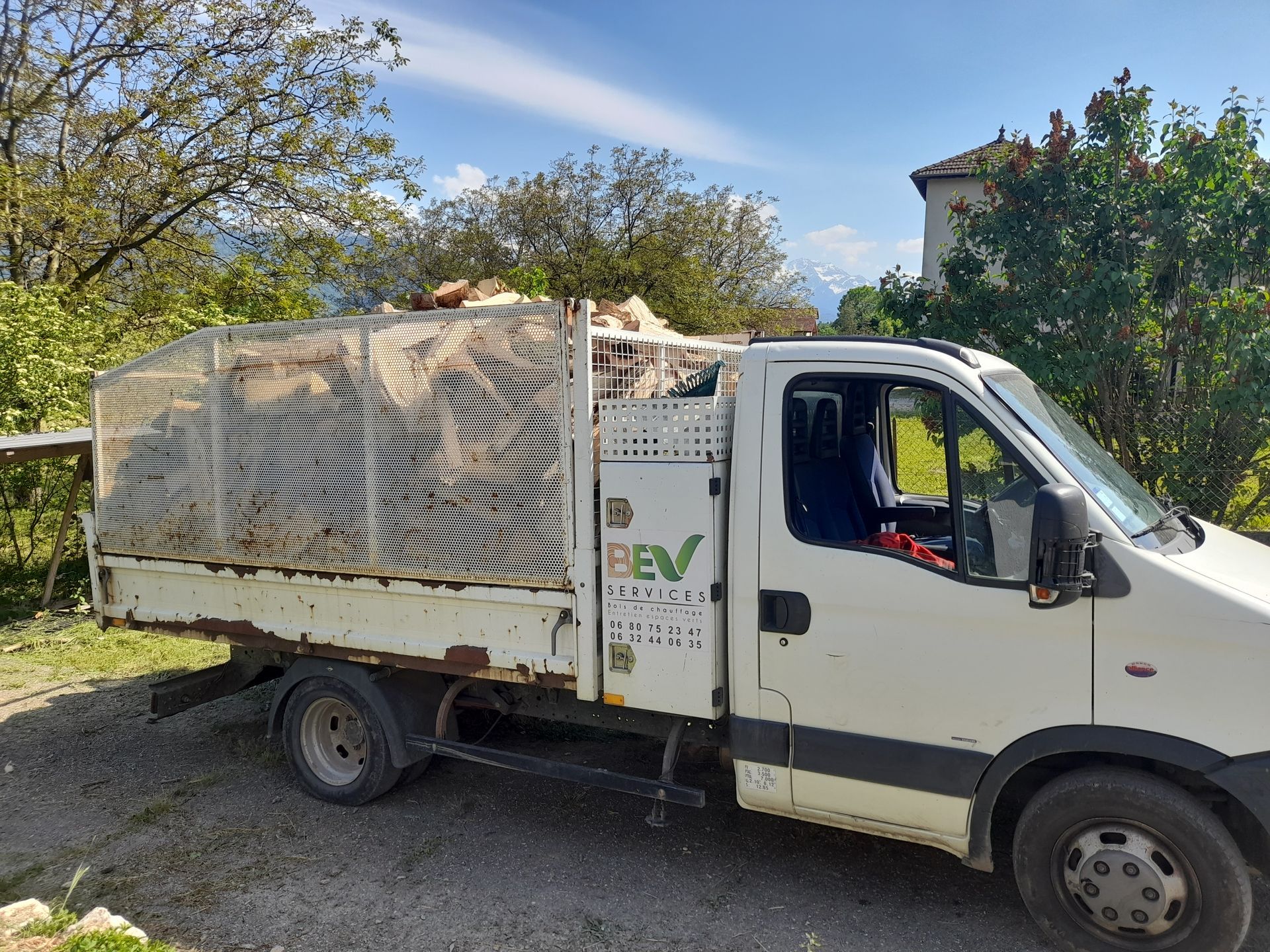 Camion blanc chargé de marchandises ; le chargement est partiellement recouvert et un bâtiment est visible en arrière-plan.