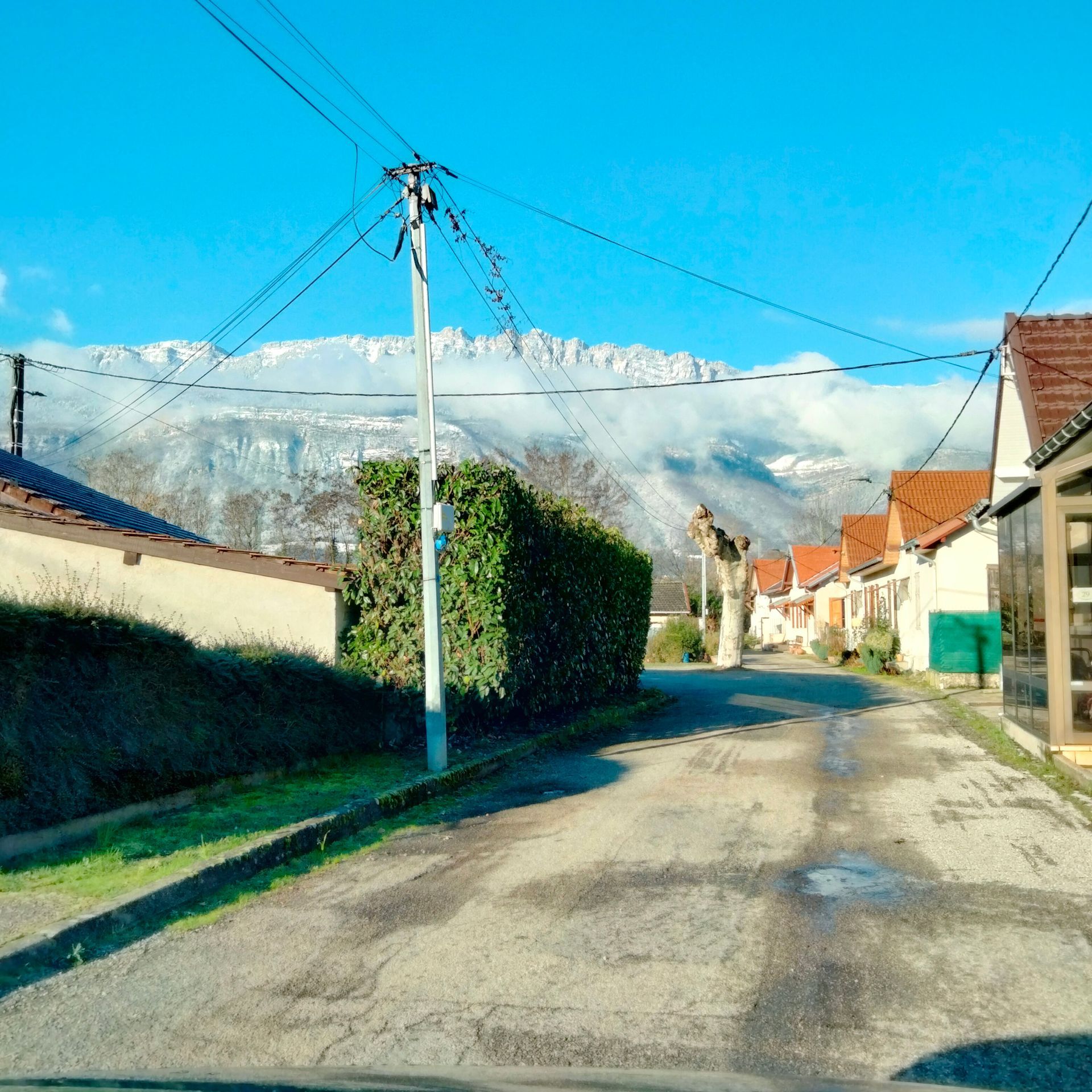 Rue d'un village avec des montagnes enneigées en arrière-plan, un ciel bleu et des maisons de part et d'autre.