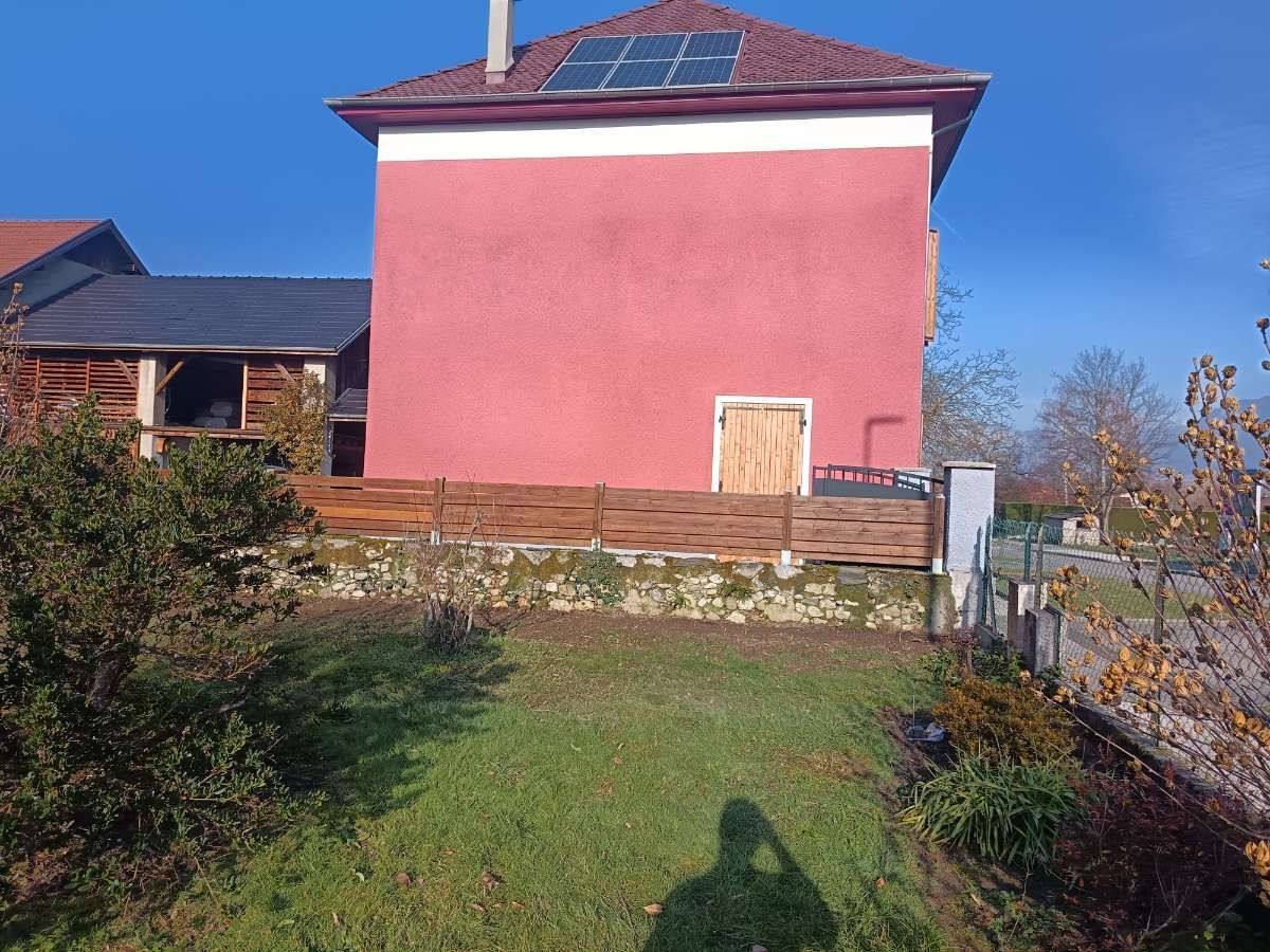 Maison rouge avec des panneaux solaires sur le toit, clôture en bois et pelouse verte par une journée ensoleillée.