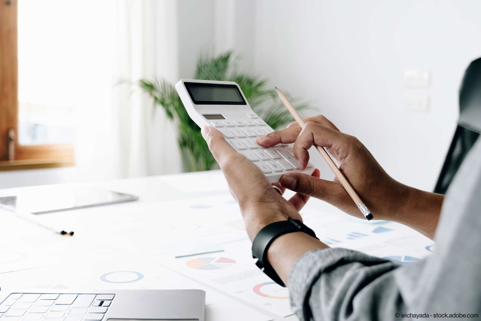 Eine Person benutzt einen Taschenrechner, während sie an einem Schreibtisch sitzt.