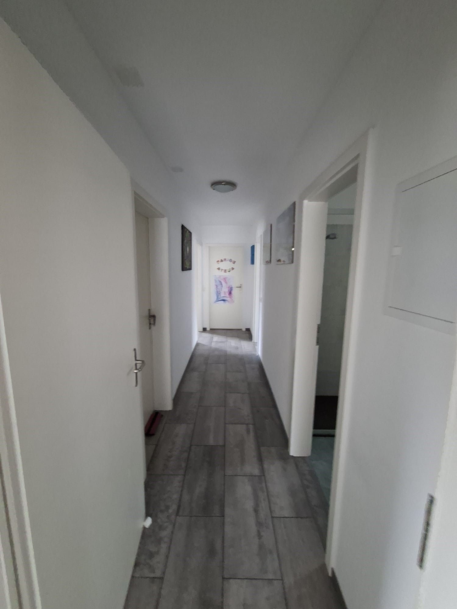 Lungo corridoio bianco con pavimento in piastrelle grigie e porte aperte su entrambi i lati.