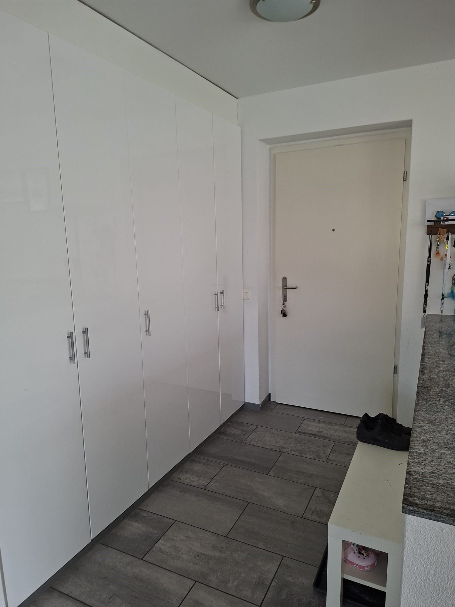 Corridoio bianco con armadi a muro, porta chiusa, piastrelle grigie sul pavimento e panca porta scarpe.