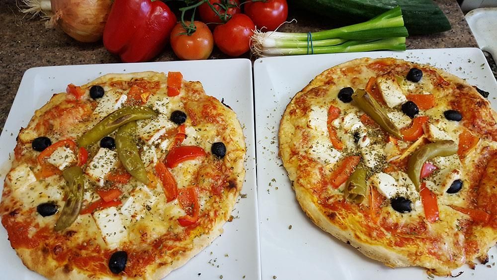 Auf einem Tisch liegen zwei Pizzen neben Gemüse.