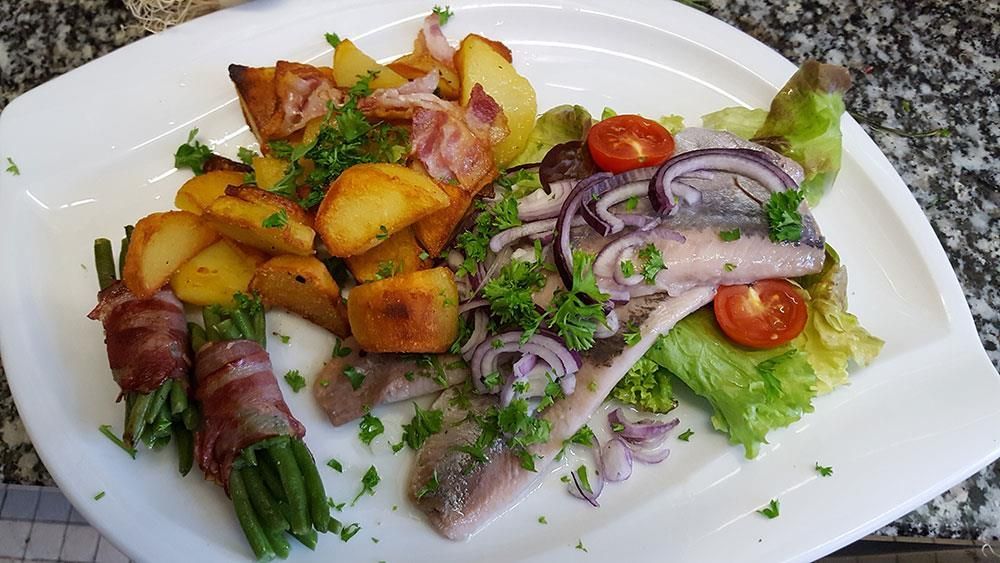 Ein weißer Teller mit Fleisch, Kartoffeln, grünen Bohnen, Zwiebeln und Tomaten.