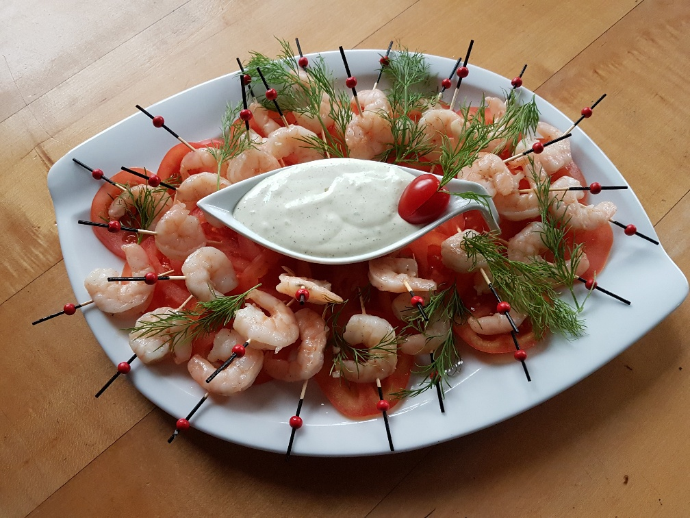Ein weißer Teller mit Garnelen, Tomaten und Dip