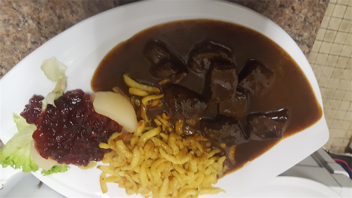 Ein weißer Teller mit Eintopf, Nudeln und Preiselbeersoße.