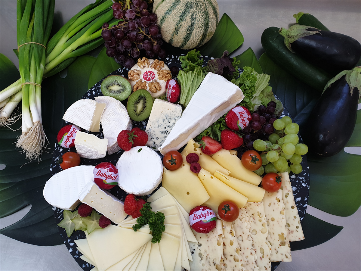 Ein Teller mit Käse, Obst und Gemüse auf einem Tisch.