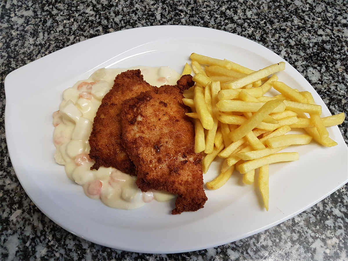 Ein weißer Teller mit frittiertem Hühnchen und Pommes Frites auf einem Tisch.