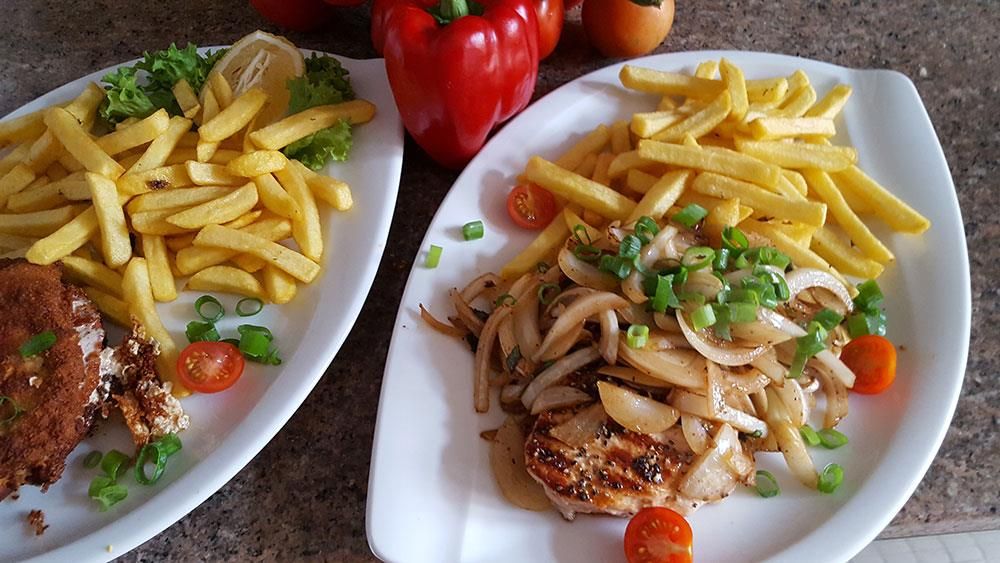 Zwei Teller mit Essen mit Pommes Frites und Fleisch auf einem Tisch