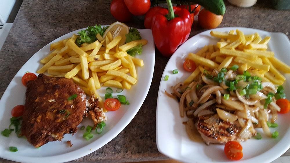 Zwei Teller mit Essen mit Pommes Frites und Fleisch auf einem Tisch