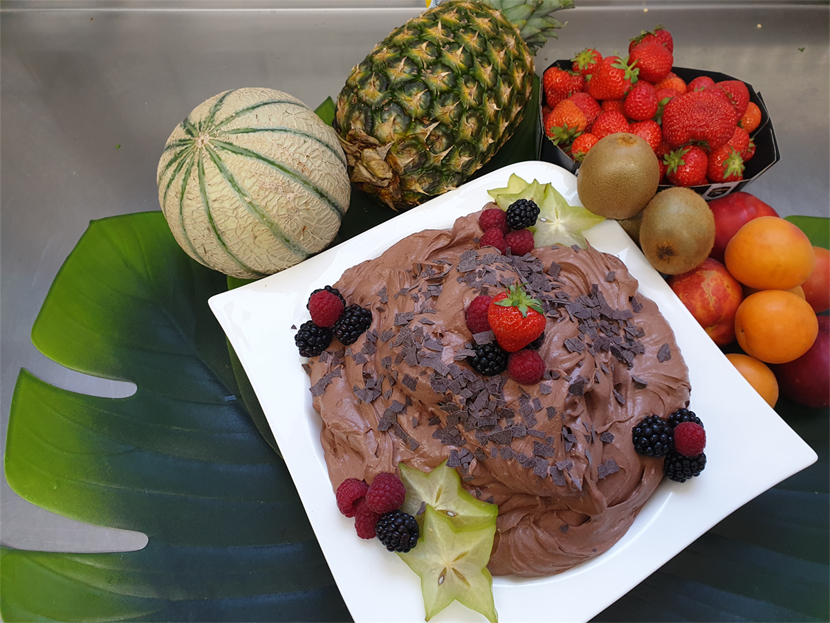 Ein weißer Teller mit Schokolade und Beeren ist von Früchten umgeben