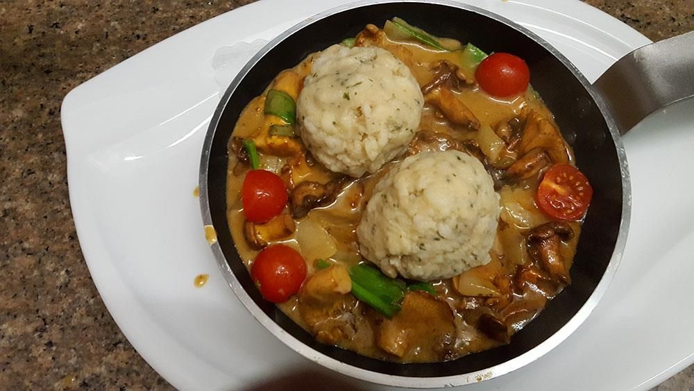 Eine Pfanne mit Essen mit Tomaten und Knödeln auf einem weißen Teller
