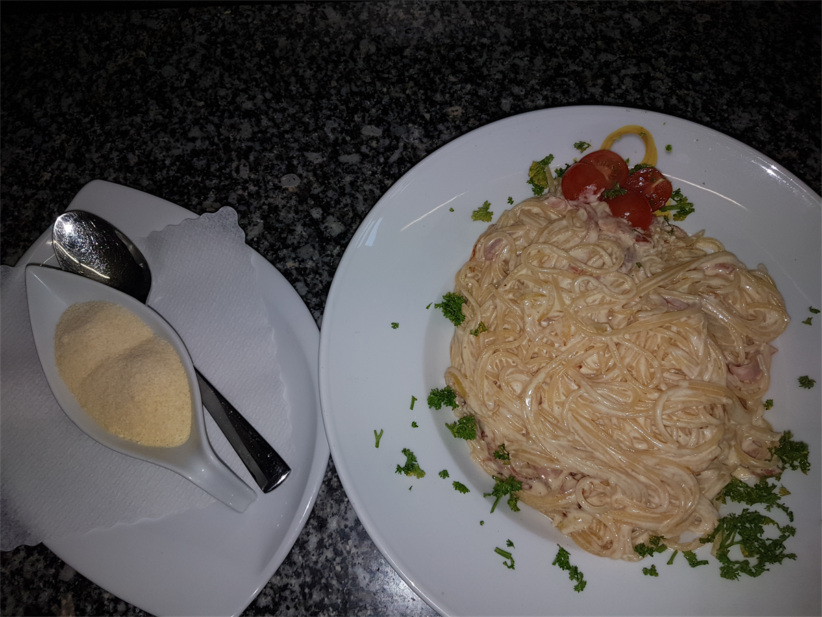 Ein weißer Teller mit Spaghetti und Tomaten neben einer kleinen Schüssel Käse.