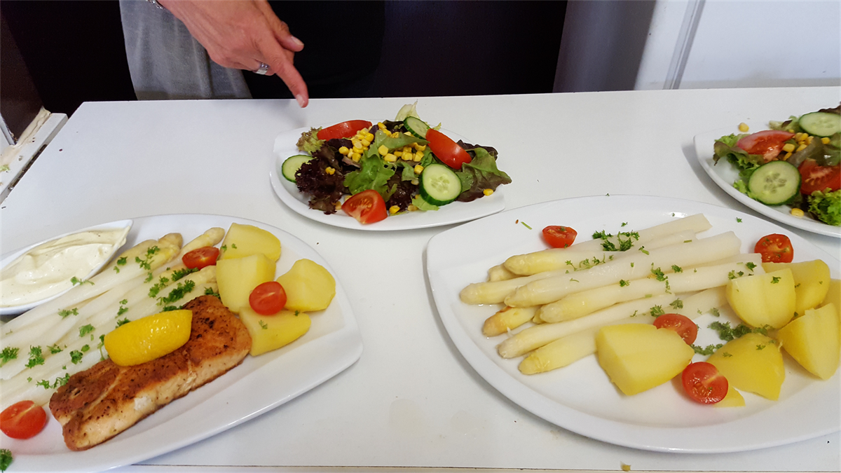 Eine Person zeigt auf einen Teller mit Essen auf einem Tisch.