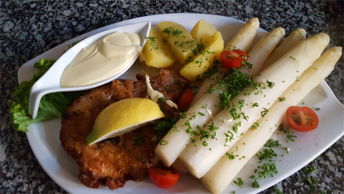 Ein weißer Teller mit Spargel, Kartoffeln, Tomaten und einer Zitronenscheibe.