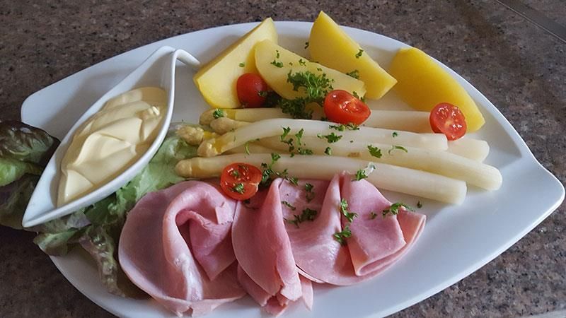 Ein weißer Teller mit Schinken, Spargel und Kartoffeln