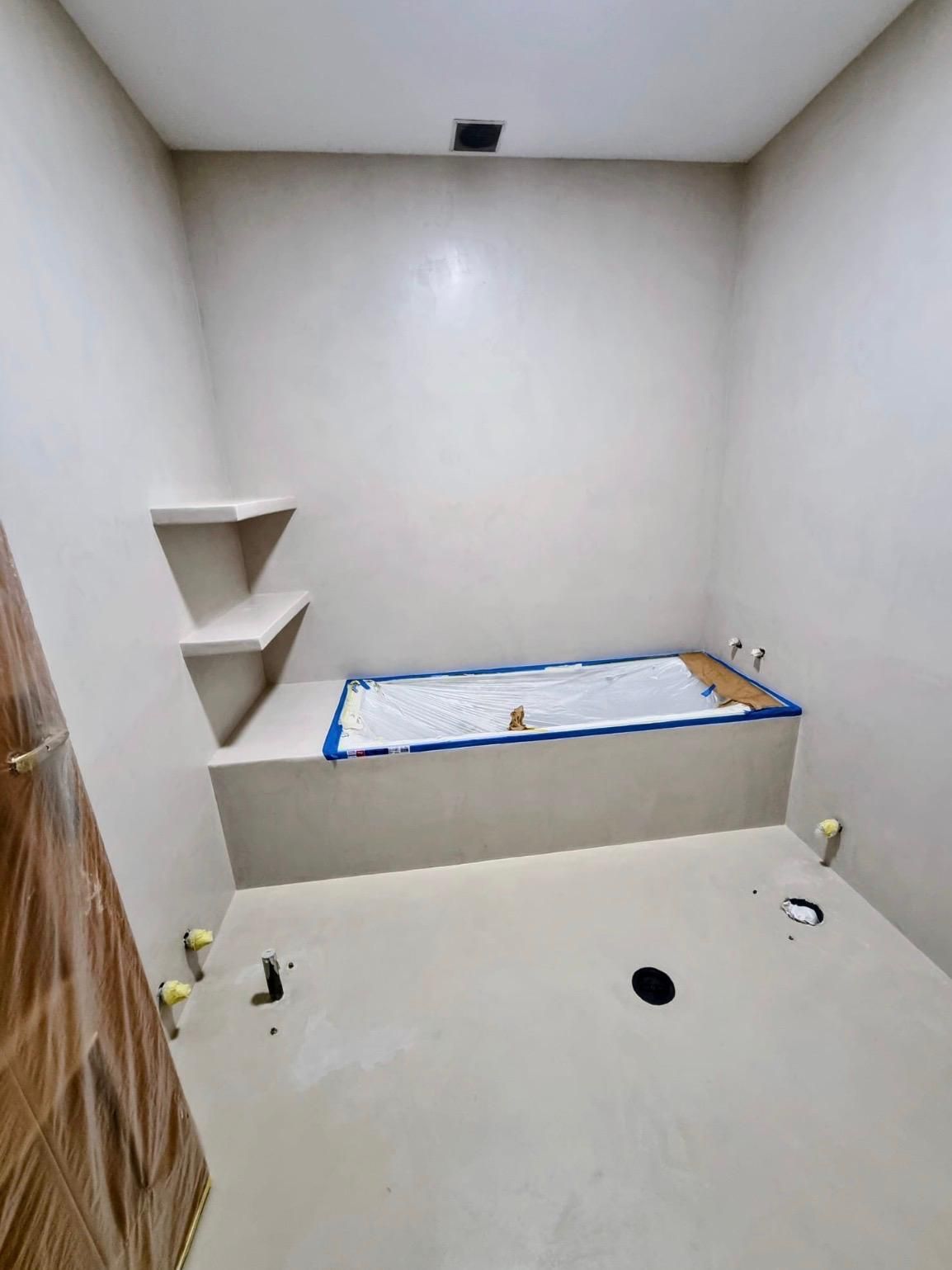 Baño vacío en construcción con paredes blancas, suelo de baldosas y un nicho empotrado para ducha o bañera.